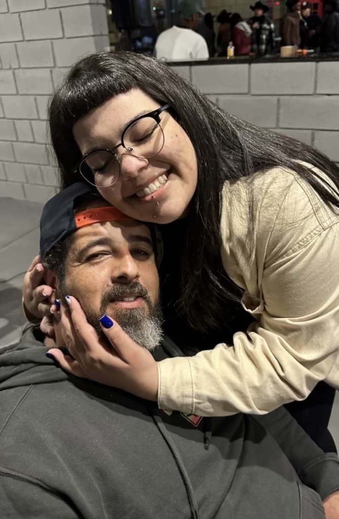Gabi de óculos abraçando o pai, Big Smoke, de barba e boné